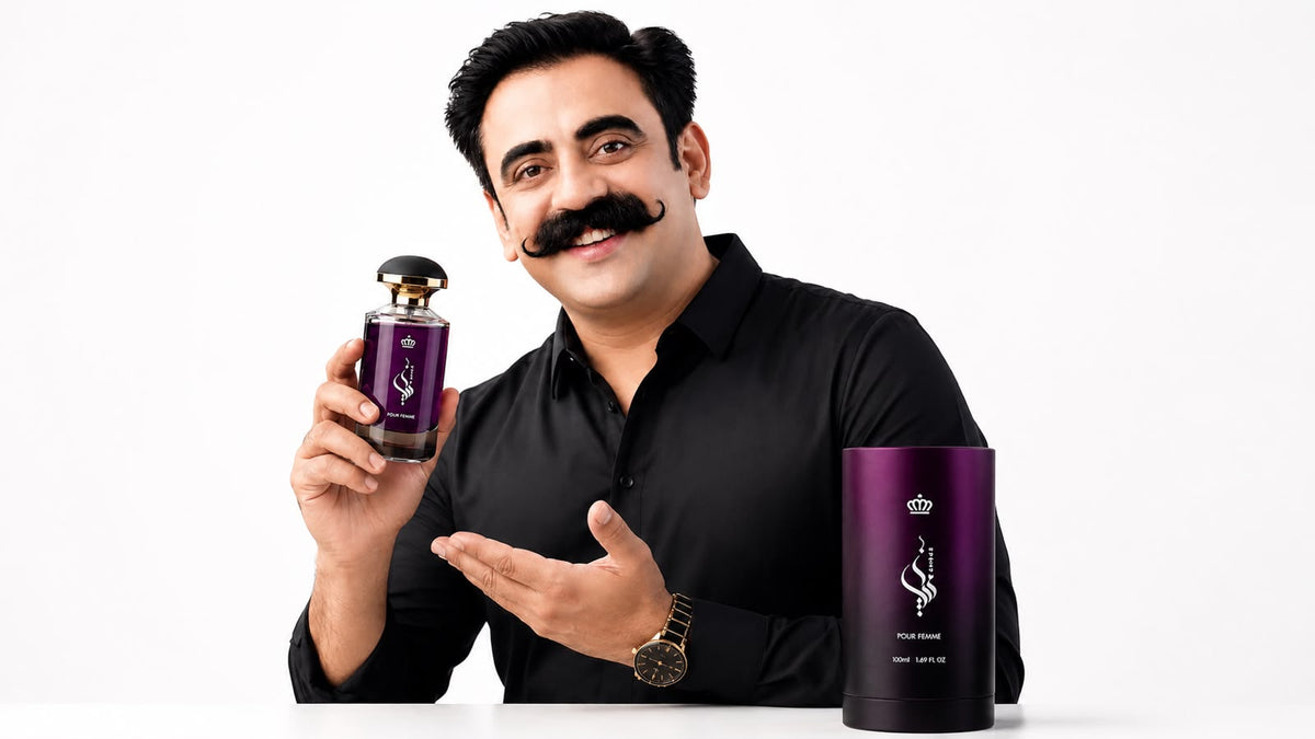 A man with a large fake mustache wearing a white shirt holds a purple cylindrical perfume bottle next to a matching purple cylindrical box on a white background.